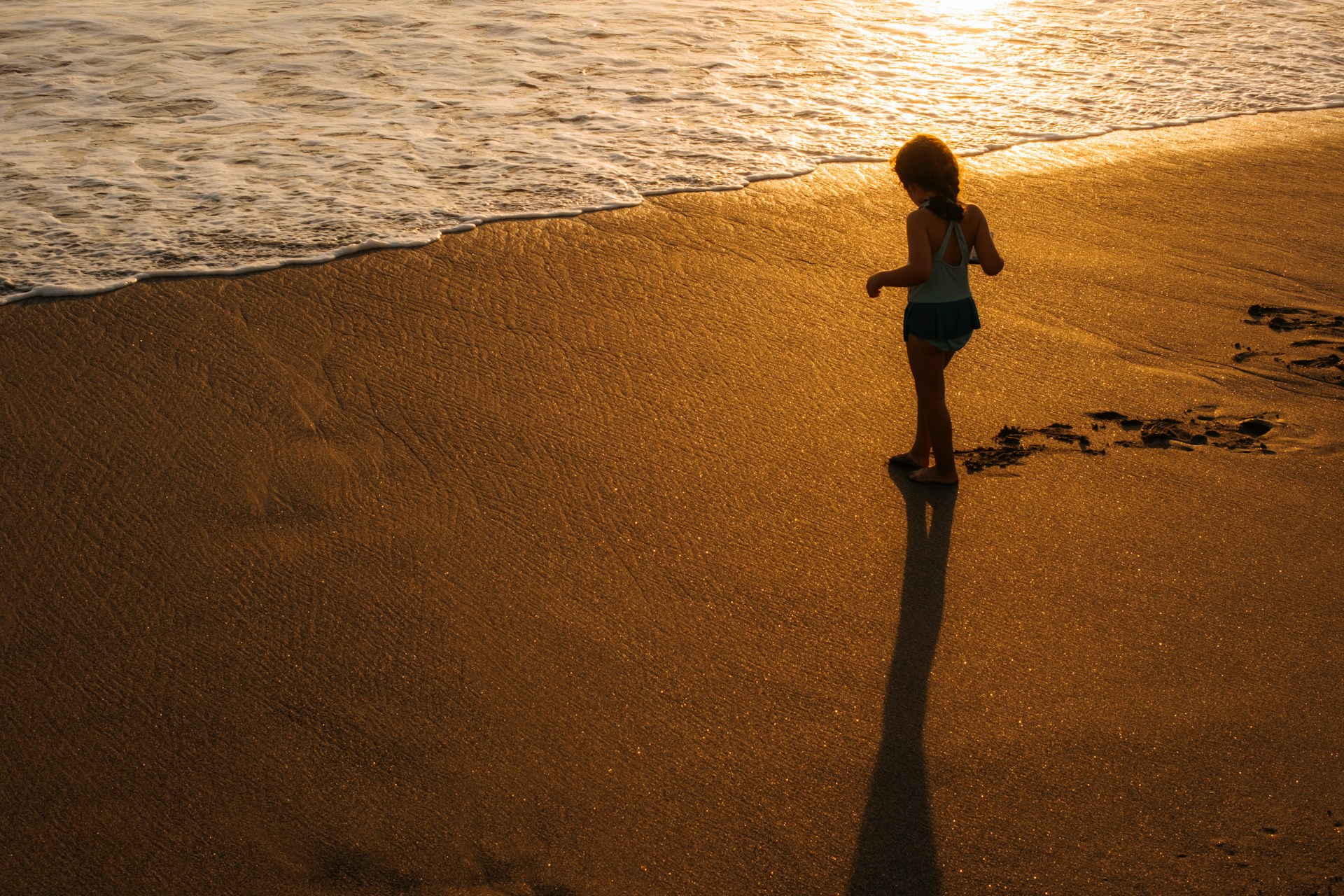 Child playing on a sandy beach at sunset—open space and warm light